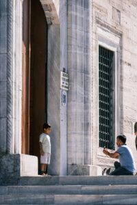 A man takes a photo of a child outside a historical stone building, capturing a candid moment.