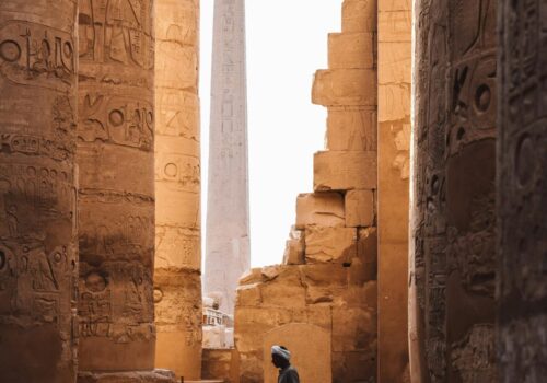 A serene view of the Karnak Temple's ancient columns and obelisk with a person walking through.